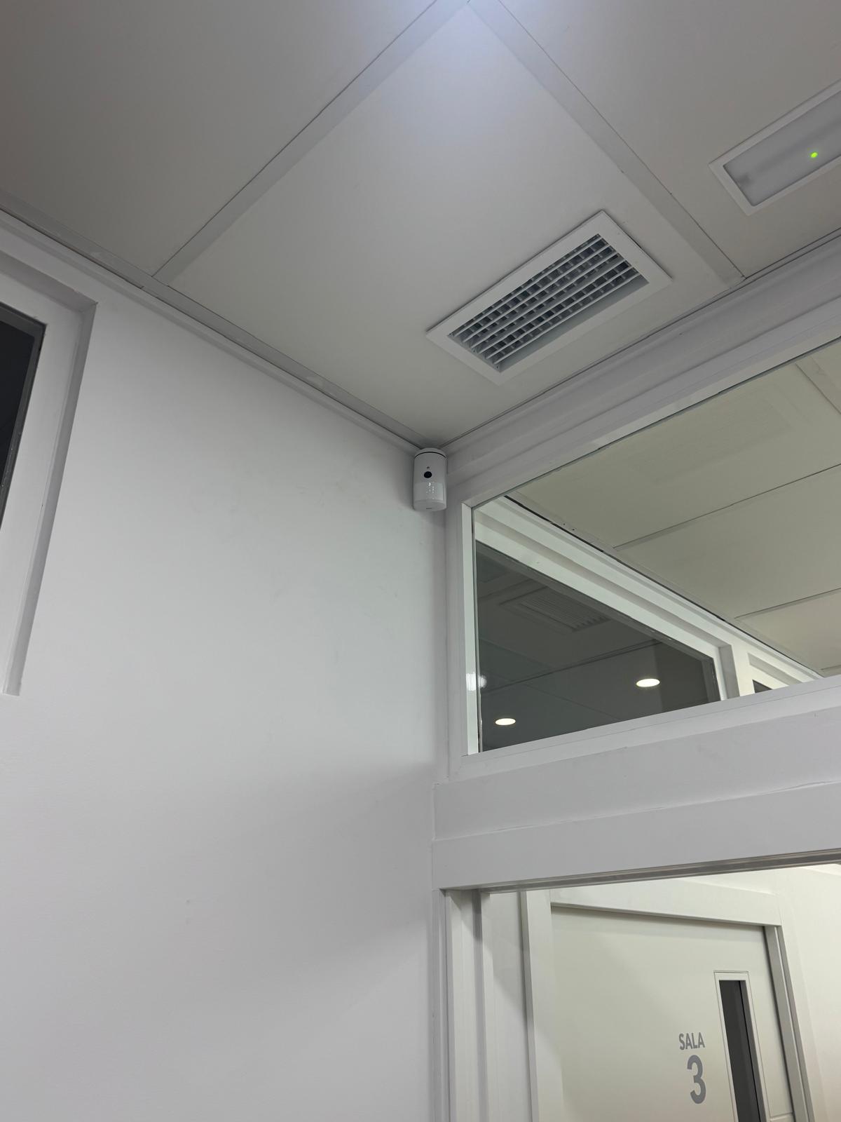 Detector de movimiento Jablotron instalado junto a la mampara de cristal de la Sala 3, en el pasillo de la clínica