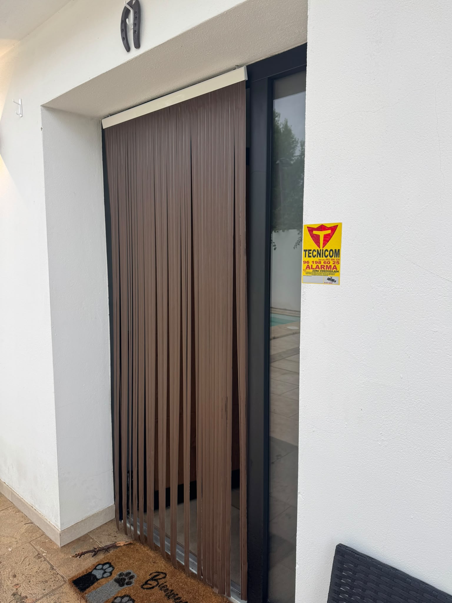 Puerta de acceso a una vivienda de Turís con el cartel de alarma de Tecnicom y la zona de piscina al fondo
